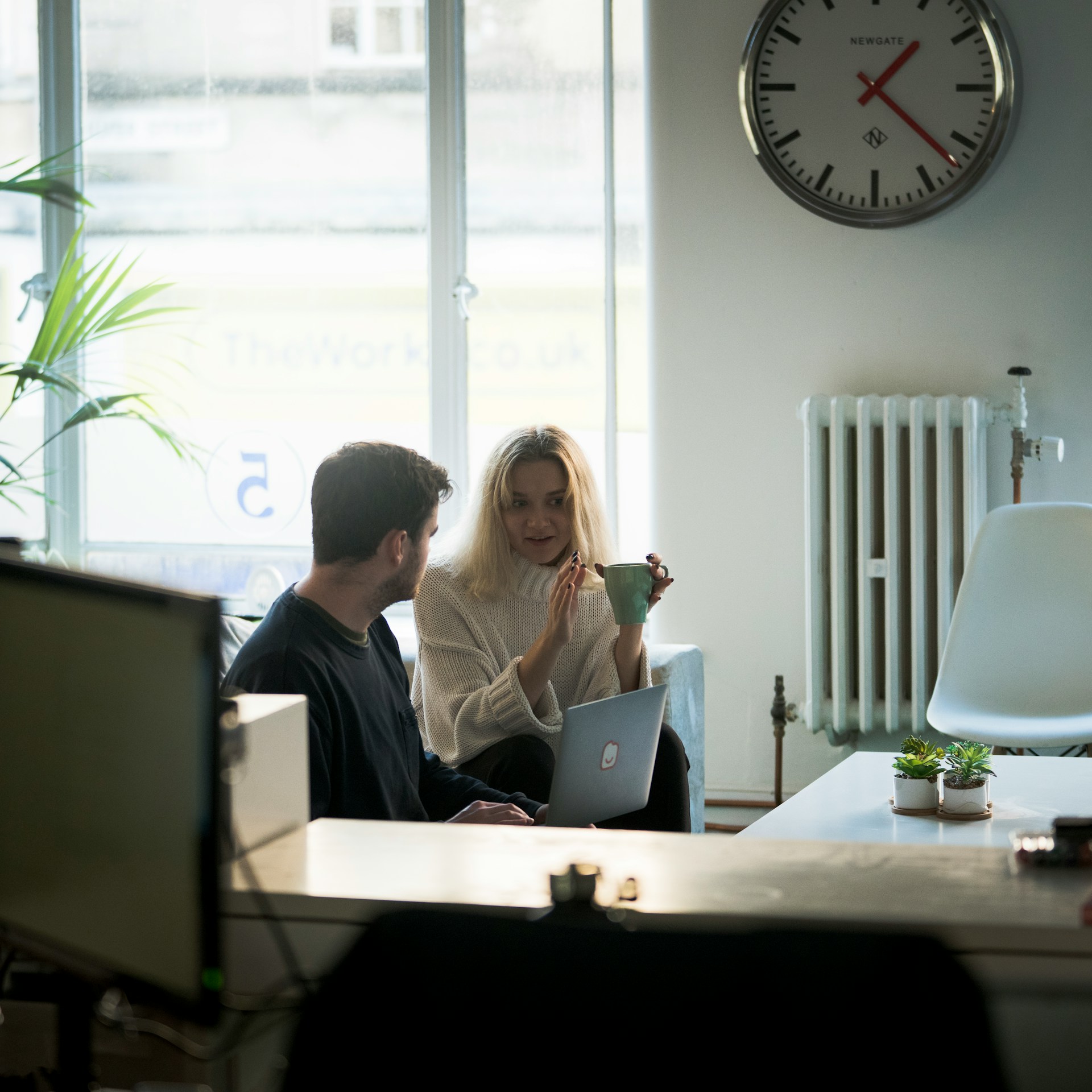 Een vervormd beeld toont mensen die aan bureaus zitten in een kantoor met grote ramen en een klok aan de muur, maar digitale haperingen verdoezelen veel details.