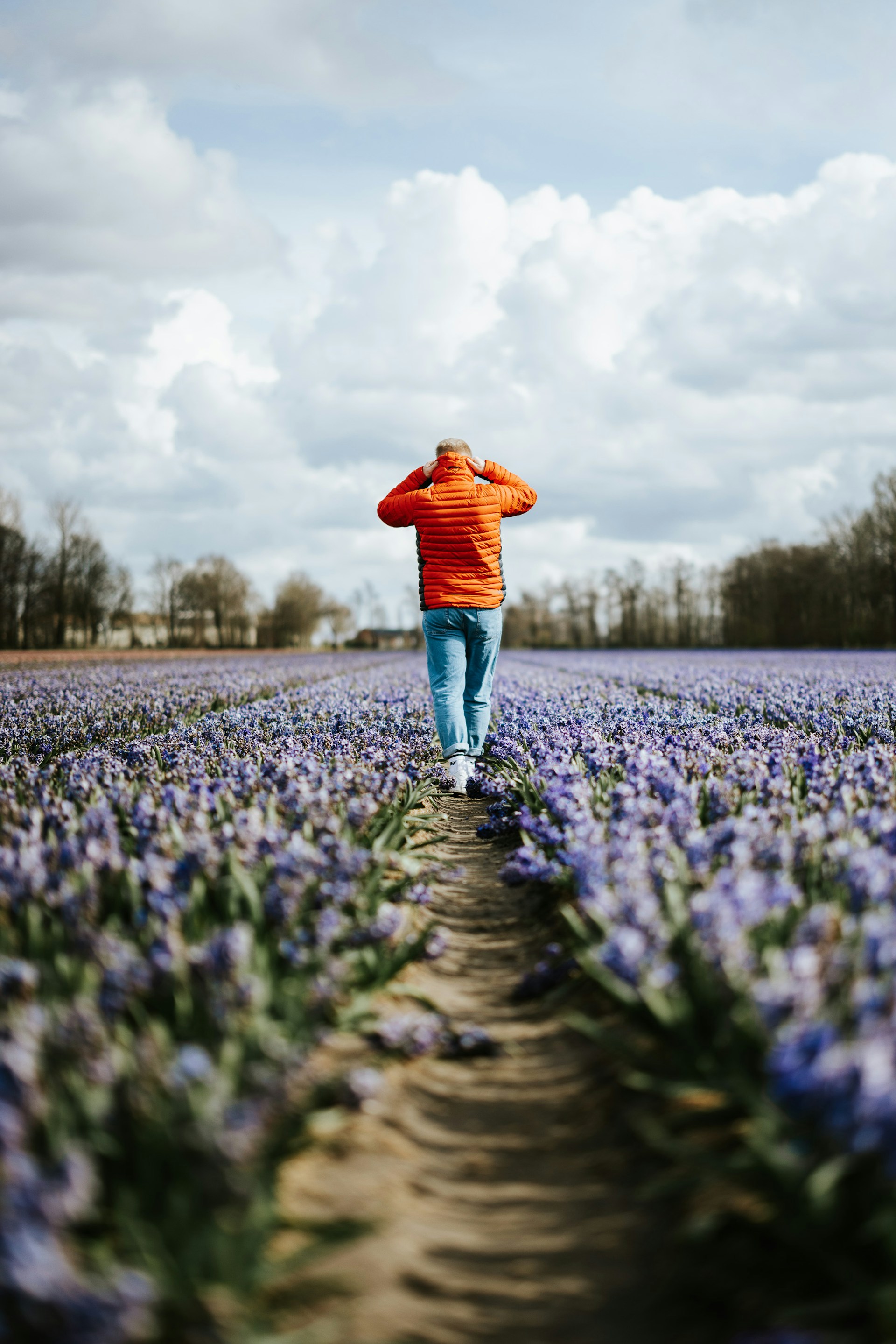 Een persoon met een fel oranje topje staat in een veld met paarse bloemen en maakt een foto. Het beeld is vervormd met diagonale digitale haperingen, waardoor de scène gefragmenteerd lijkt.