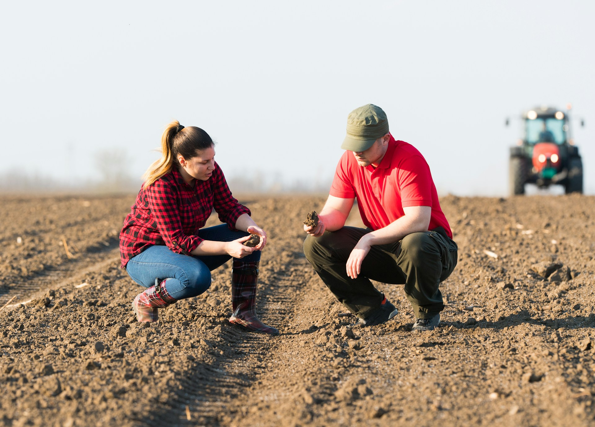 Een vervormd, vervormd beeld van twee mensen die gehurkt in een omgeploegd veld de grond onderzoeken. De achtergrond is effen en het beeld is gepixeld met digitale artefacten.